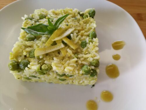 Un piatto di risotto cremoso con piselli verdi, guarnito con scorze di limone e foglie di basilico fresco su un piatto bianco.
