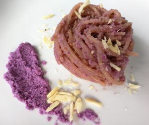 Un nido di spaghetti conditi con un pesto viola di cavolo rosso, guarnito con scaglie di mandorle su un piatto bianco.