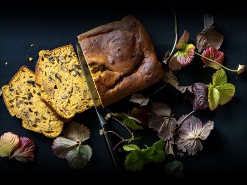 Un pane alla zucca tagliato a fette su un fondo scuro, decorato con foglie autunnali.
