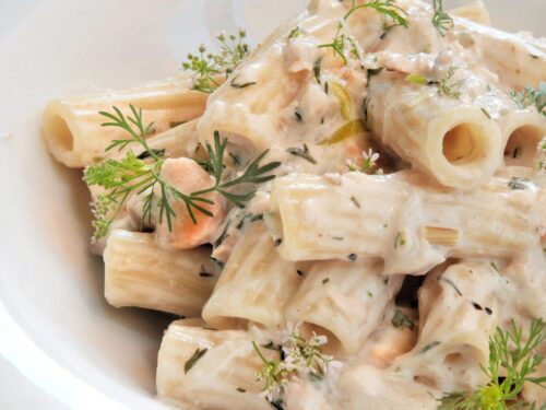 Un piatto di rigatoni conditi con una cremosa salsa al salmone e latte di cocco, guarniti con erbe fresche.