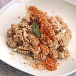 Un piatto di radiatori integrali conditi con crema di caprino, mandorle a scaglie, una foglia di menta e una spolverata di polvere di mais alla paprika.