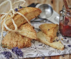 Scones triangolari al limone e lavanda impilati su un tovagliolo decorato con fiori di lavanda freschi.