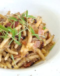 Un piatto di trofie integrali condite con radicchio, speck e guarnite con germogli freschi.
