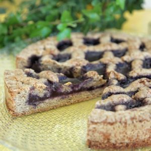 Una fetta tagliata di Linzer Torte con confettura scura su un piatto di vetro decorato.