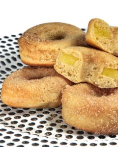 Un gruppo di ciambelle vegane alle mele cosparse di zucchero e cannella su un piatto a pois.