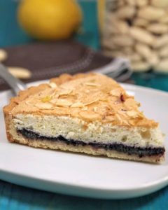Una fetta di crostata con base ai mirtilli e strato superiore di frangipane al limone guarnita con mandorle a lamelle.