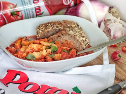 Un piatto di trippa alla romana servito con fette di pane ai cereali, accompagnato da una bottiglia di passata di pomodoro Pomì.