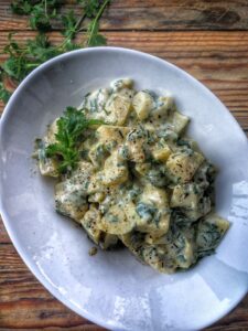 Una ciotola di insalata di patate tedesca condita con erbe aromatiche e una salsa cremosa, servita su un tavolo di legno.