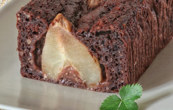 Una fetta di torta al cioccolato con una pera intera all'interno, servita su un piatto chiaro.