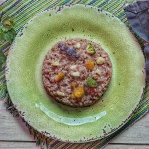 Un piatto di risotto colorato guarnito con cimette di cavolfiore viola, giallo e verde, servito su un piatto verde in ceramica.