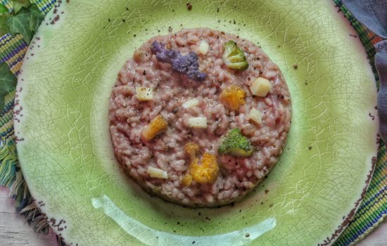 Un piatto di risotto al radicchio guarnito con cimette di cavolfiore colorato e cubetti di formaggio servito su un piatto verde crepato.