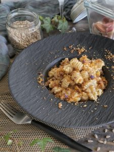 Un piatto di pasta radiatori condita con cavolfiore e una granella croccante, servito in un piatto fondo nero su un tavolo di legno.