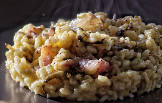 Un primo piano di un risotto cremoso condito con carciofi a fettine e pezzi di guanciale croccante.