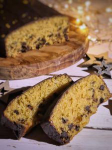 Due fette di Pan d'Arancio vegano con gocce di cioccolato posizionate su un piano di legno chiaro accanto a decorazioni a forma di stella.