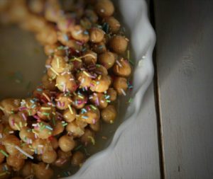 Primo piano di una cicerchiata, tipico dolce italiano composto da palline di pasta fritte e ricoperte di miele, decorate con confettini colorati in una pirofila bianca.