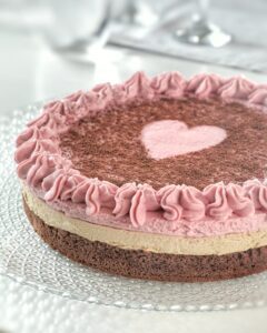 Una torta a tre strati con base al cioccolato, strato centrale al caffè e copertura di crema ai lamponi decorata con un cuore centrale.