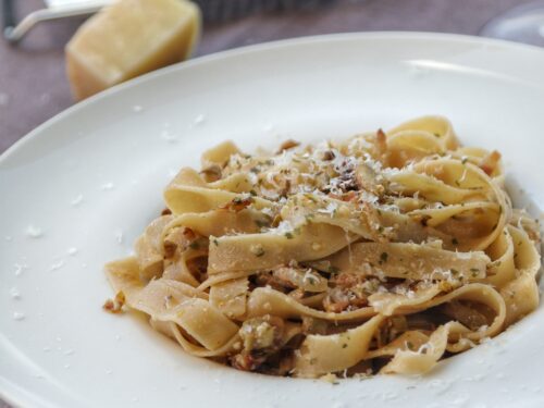 Un piatto di fettuccine integrali condite con carciofi e guanciale, guarnite con una spolverata di formaggio grattugiato.