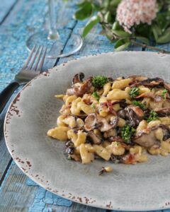 Un piatto di spätzle conditi con funghi, pancetta e prezzemolo servito su un piatto di ceramica grigia.