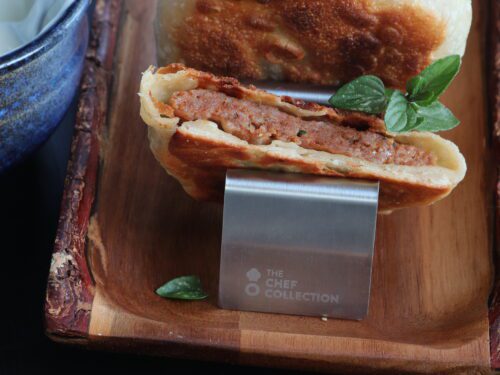 Un medaglione turco ripieno di carne dorato e croccante, servito su un supporto metallico sopra un vassoio di legno.