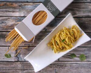 Un piatto di tagliatelle al limone condite con pepe e basilico fresco, servite accanto alla confezione originale di pasta su un tavolo di legno.