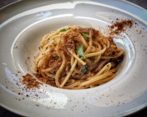 Un piatto di pasta lunga condita con melanzane e guarnita con mollica tostata e basilico fresco.