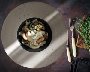 Un piatto di gnocchi conditi con una salsa cremosa bianca, serviti in un piatto fondo dal bordo ampio su un tavolo scuro.