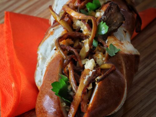 Un panino farcito con funghi sfilacciati e prezzemolo fresco su un tagliere di legno.