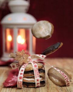 Una pila di biscotti Elisenlebkuchen legati con un nastro natalizio, con altri biscotti che sembrano fluttuare e una lanterna accesa sullo sfondo.