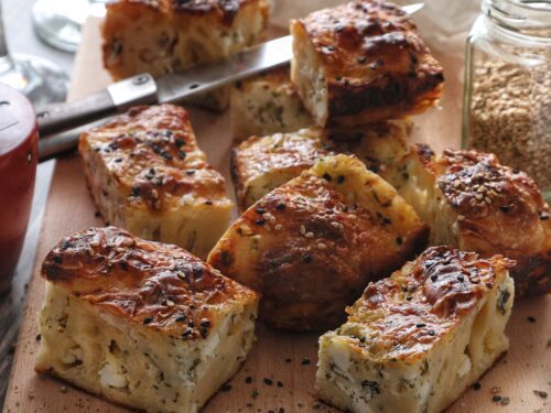 Pezzi di börek dorati e croccanti, guarniti con semi di sesamo e nigella, disposti su un tagliere di legno.