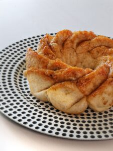 Un monkeybread vegano lucido e dorato, servito su un piatto decorato con un motivo a pois neri.
