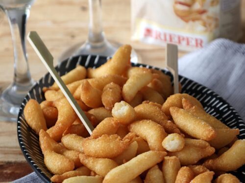 Un piatto ovale nero con decorazioni bianche riempito di snack fritti a forma di mezzaluna, con due stecchini di legno inseriti.