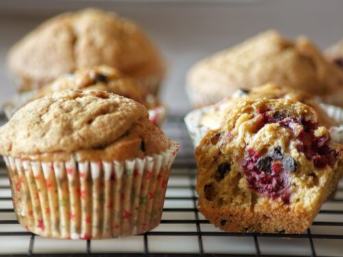 Muffin appena sfornati su una griglia di raffreddamento, con uno tagliato a metà che mostra l'interno con lamponi e gocce di cioccolato.