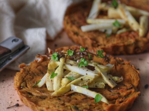 Due frittatine vegane rotonde guarnite con asparagi bianchi a listarelle e rametti di timo fresco su un tagliere di legno.