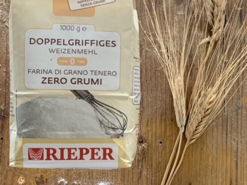 Una confezione di farina Rieper di tipo 0 accanto a due spighe di grano su un tavolo di legno rustico.