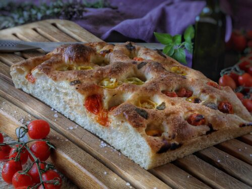 Una focaccia rettangolare appena sfornata, guarnita con pomodorini rossi e gialli, posizionata su un tagliere di legno.