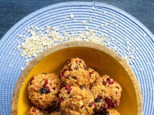 Biscotti all'avena con frutti rossi disposti in una ciotola di legno su una tovaglietta blu.