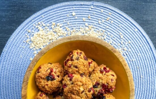 Biscotti all'avena con frutti rossi disposti in una ciotola di legno su una tovaglietta blu.