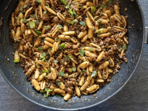 Cavatelli saltati in padella con lenticchie, pezzi di salsiccia e foglie di menta fresca.