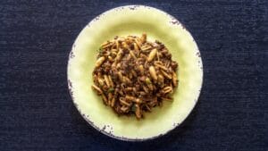 Un piatto di cavatelli conditi con salsiccie, lenticchie e aglio nero servito su un piatto giallo chiaro con bordo decorato.