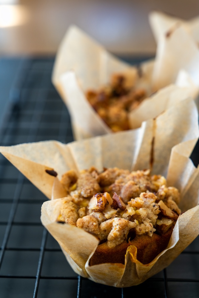 Muffin appena sfornati con una croccante copertura di crumble alle noci, disposti su una griglia di raffreddamento.