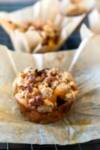 Un muffin appena sfornato con una copertura croccante di noci, servito in un pirottino di carta su una griglia.