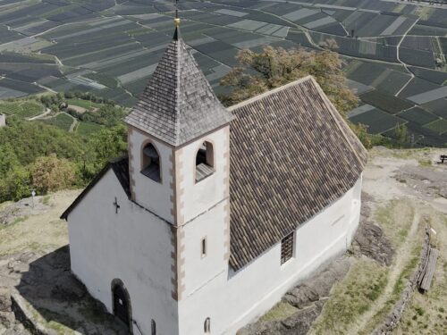 La chiesetta di Sant'Ippolito sul colle sopra Narano, a Tesimo, con i meleti della piana di Lana sullo sfondo, vista dal drone